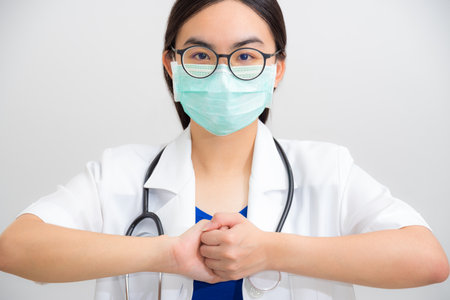 Portrait beautiful Asian woman doctor with stethoscope and mask to protect Corona Virus clasp hand gesture of beg for help cooperation, work together confederate to stop the epidemic COVID 19 conceptの写真素材