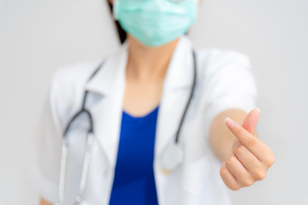 Woman doctor give a hand with fingers in the shape mini heart, wear a mask to protect Coronavirus, Show sign language as a symbol of giving love, Promise to take good care and attention is a conceptの写真素材