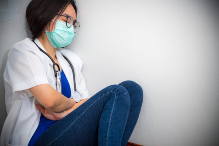 Asian young woman doctor wear mask to safety Coronavirus sit on the corner floor sleeping with exhaustion from overwork concept take care yourself is to help physician stop the epidemic Covid-19 virusの写真素材