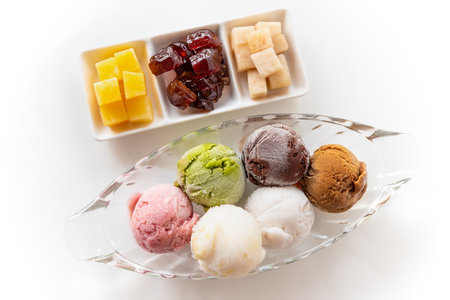 Top view multi-colored ice cream in a clear dish and sweet processed fruit for eating together in vintage Thai style, Set of colorful ice cream scoops of different colors on the white table backgroundの写真素材