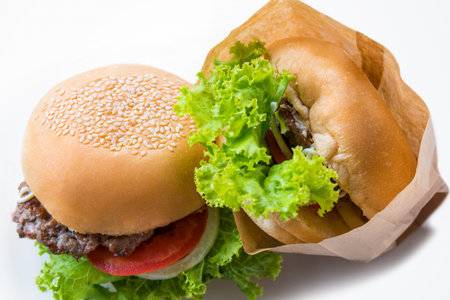 Closeup top view two hamburger made from pork or beef, green lettuce bread onion white sesame and tomato in a paper bag on a white table background made at home. Burger is delicious American fast foodの写真素材