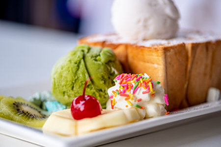 Closeup Honey Toast bread served with green tea and coconut milk ice cream scoop, decorate with cherry, apple, kiwi fruit, and cream sugar topping sprinkle on a white dish sweet cool snack in summerの写真素材