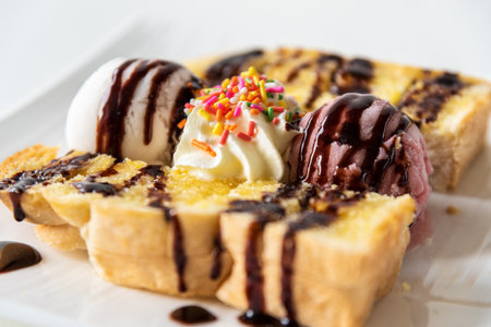Closeup side view Honey Toast bread and Chocolate brown Ice cream scoop topped with chocolate syrup decorate with a chocolate tablet in a white plate on the table sweet cool dessert in summerの写真素材
