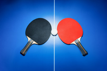 Top view black and red table tennis racket and a white ball on the blue table with a bright spotlight, Two table tennis paddle is a sports competition equipment for indoor exerciseの写真素材