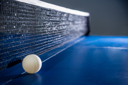 Closeup one white ball on the blue table with a black net, Table tennis paddle is a sports competition equipment indoor activity and exercise for concept backgroundの写真素材