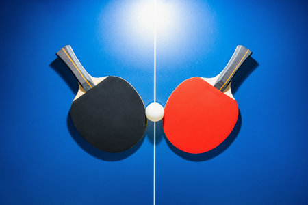 Top view black and red table tennis racket and a white ball on the blue table with a bright spotlight, Two table tennis paddle is a sports competition equipment for indoor exerciseの写真素材