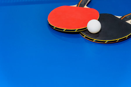 Black and red table tennis racket and a white ball on the blue table, Two table tennis paddle is a sports competition equipment for indoor exerciseの写真素材