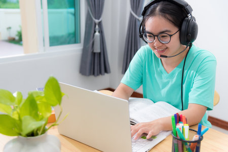 Portrait Asian young woman student with glasses headphones to study class college online learning internet education teenage girl is smiling use laptop keyboard looking computer work remotely at homeの写真素材