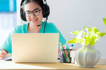 Asian young woman portrait student with glasses headphones happy study smile looking up online class college learning internet education, Teenage girl work distance on a laptop computer from homeの写真素材