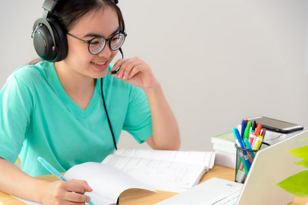 Asian woman looking to talk video conference calling on a laptop computer girl students speak respond with headset microphone class university learning internet online distance education from homeの写真素材