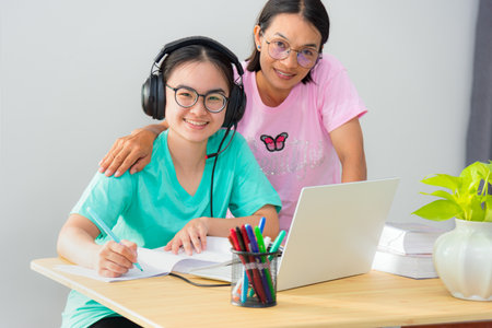 Happy family two Asian woman looking up mother parent is a teacher advice instruction daughter teenage girl student online study use a laptop computer education from university class learning at homeの写真素材