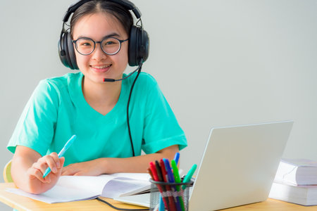 Portrait Asian young woman student glasses headphones sitting happy study smile looking up online class college learning internet education, Teenage girl work distance on a laptop computer from homeの写真素材