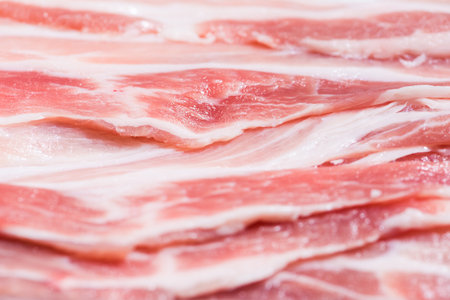 Close up top view pack bacon, pieces raw meat of fresh red pork with white fat slices are sliced into thin strips stacked on top of each otherの写真素材
