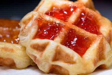 Close up of fresh waffles topped with delicious sweet strawberry jam and pineapple jam on top. Making homemade food or dessert at homeの写真素材