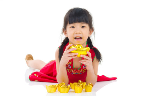 China girl in traditional Chinese  dress greeting, holding a gold ingot lying down in the studioの写真素材
