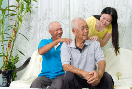 Asian old man shoulder pain, sitting on sofa , grandchild and son massaging their father and grandfather shoulder. Chinese family, senior retiree indoors living lifestyle at home.の写真素材