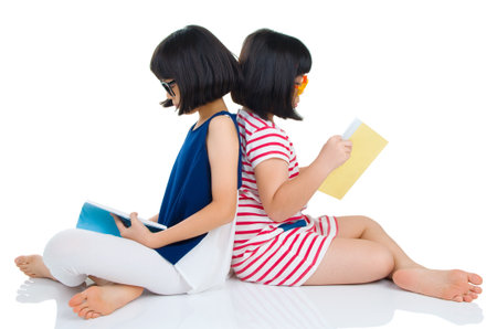 Asian girls wearing spectacles sitting on the floor with booksの写真素材