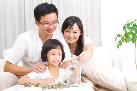 Asian mother and her kid putting coins together into the glass bottleの写真素材