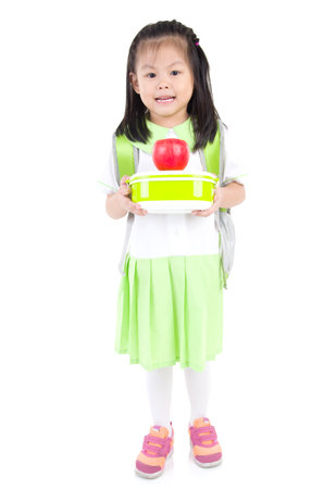 Asian primary school girl holding lunch box and apple. Healthy eating concept for schoolchild.の写真素材