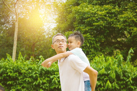 Asian father giving piggyback ride to his son in the evening sunshineの写真素材