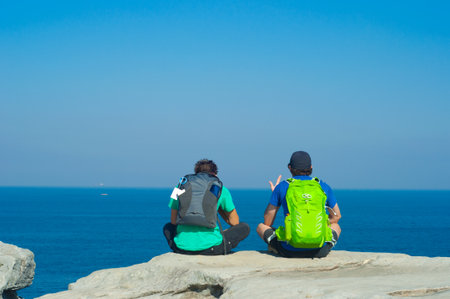 Portrait from behind of young men sitting and looking on Sea with backpack. Concept for travel or...