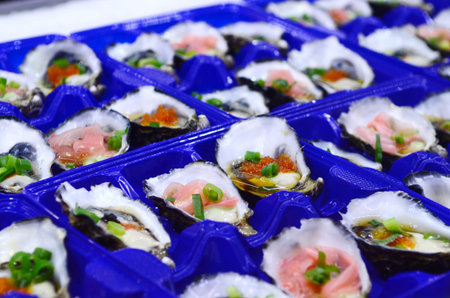 Close-up of fresh oysters mixed with ponzu sauce,ginger,vasabi sauce,and salmon caviar in trays in...