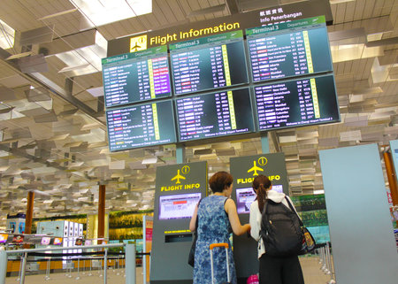 Singapore - Jun 27, 2017 : Flights information board and machine at Changi airport terminal 3.Young girl with her mother touching self check in kiosks interactive screen to check in online.のeditorial素材