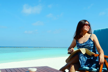 close-up portrait of a beautiful asian girl with long hair on a background of blue sea and sky with clouds on a sunny day, lifestyle, posing and smiling.の写真素材