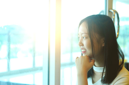 Side view portrait of a young asian girl looking through a window at restaurantの写真素材