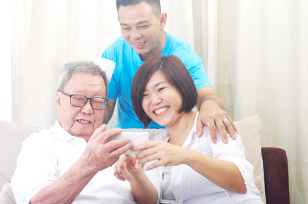 Modern technology, age and people concept. Asian senior man with his daughter and son taking selfie, using smartphone, self photographing