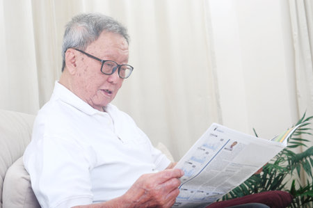 Asian senior man reading newspaper at homeの写真素材