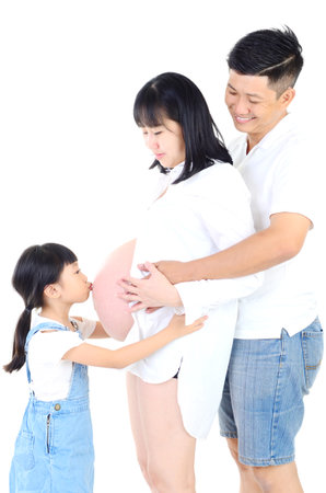 Little asian girl kissing her pregnant mother belly and smiles at homeの写真素材