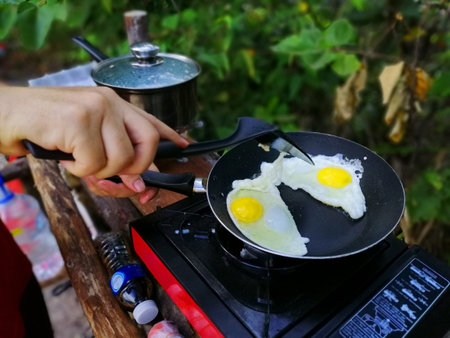 Woman cooking breakfast on campfire in cast iron pan with selective focus.の写真素材