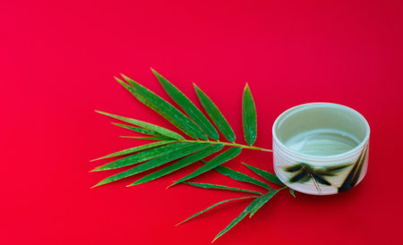 A cup of tea with a twig of bamboo leaves on a bright red background.の写真素材