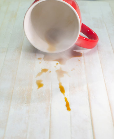 A picture of a coffee drink spilled out of a red glass on a white wood floor
