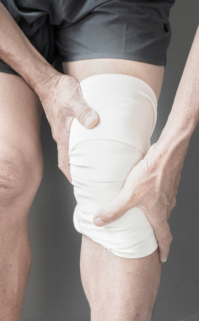 The image of the person holding the muscles around the knee with a bandage On a gray background with...