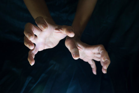 Hand gestures performing magic on a black background against light and dark shadow.の写真素材