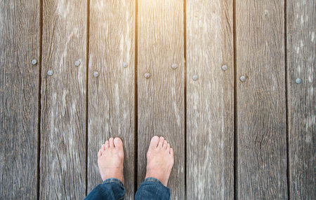 Two bare feet stand on an old wooden bridge.の写真素材