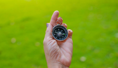 Female hand holding a compass against the background of the green grass.の写真素材