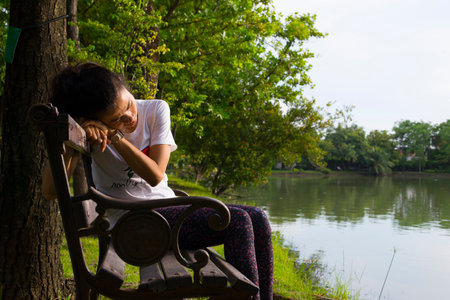 Asian woman sitting on a chair by the lake in the park.の写真素材