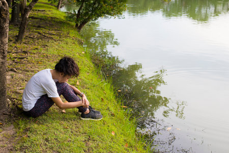 Asian woman sitting on the grass beside the river and looking at the lake.の写真素材
