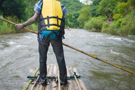 Man with yellow life jacket standing on a wooden raft on the river.の写真素材