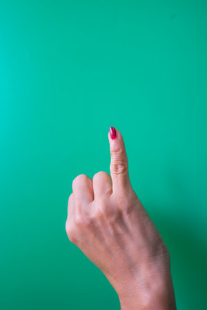 Female hand pointing at something on a green background with copy space.