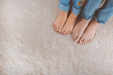 Two pairs of bare feet in jeans resting on a soft carpetの写真素材
