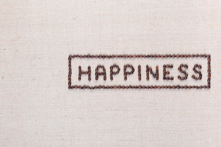 Happiness sign enclosed in a rectangle made from coffee beans on creamy linea canvas, shot from above, aligned middle right.の写真素材