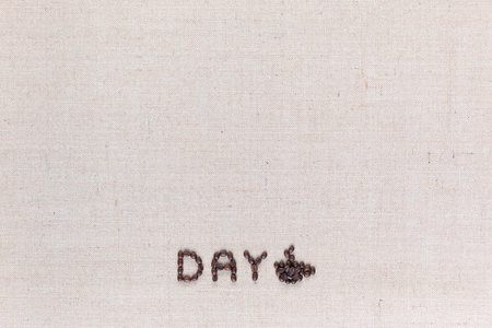Day logo letters with a cup of coffee to the right, shot from above on creamy linen canvas aligned bottom center.の写真素材