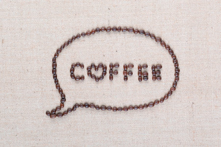 Coffee word from coffee beans enclosed in a chat cloud on creamy linen canvas shot from above, aligned close up.の写真素材