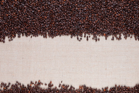 A lot of coffee beans on creamy linen texture arranged to let open space at the bottom.の写真素材