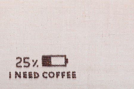 Low level battery with 'I need coffee' sign made from roasted coffee beans on creamy linen canvas, shot from above, aligned bottom left.の写真素材
