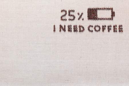Low level battery with 'I need coffee' sign made from roasted coffee beans on creamy linen canvas, shot from above, aligned top right.の写真素材